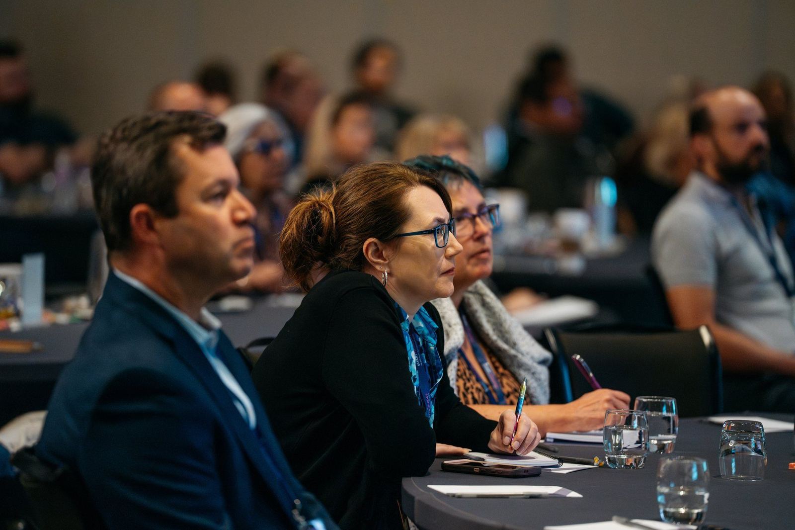 Attendees seated at round tables taking notes during a session
